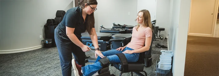A young woman using a knee decompression device with the help of a clinic employee